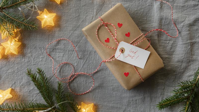 Närbild på en inslagen julklapp, med granris och julbelysning runt om.