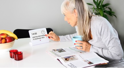 Bild på en person som sitter vid ett bord och trycker på ett kognitivt hjälpmedel memoday.