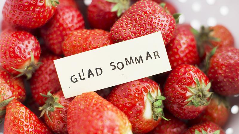 Närbild på en hög med jordgubbar och en skylt som lyder "GLAD SOMMAR".