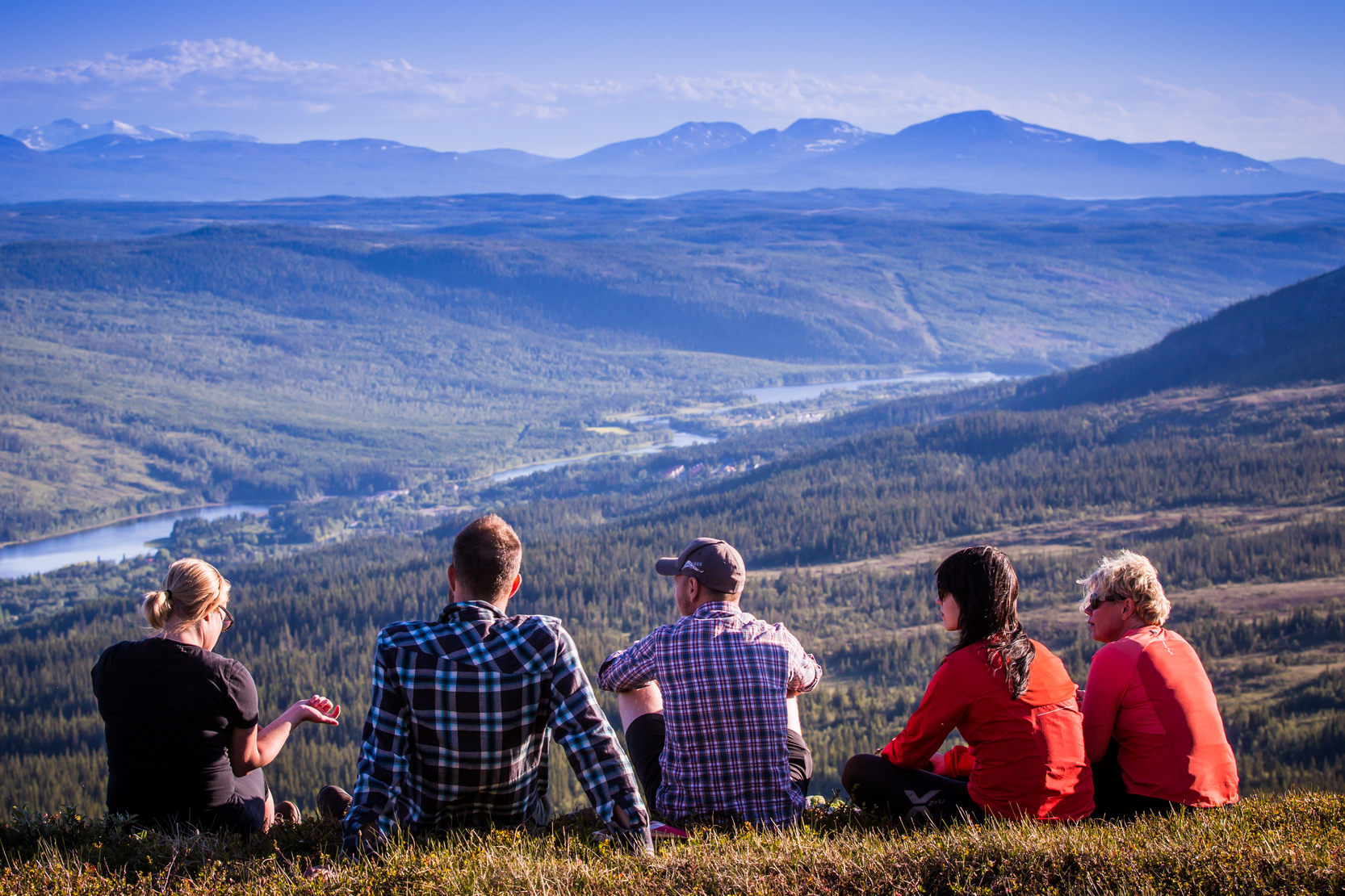 Personer som sitter ned i gräset och tittar utöver fjället och vattnet i dalen.