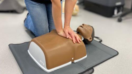 En utbildningsledare inom hjärt- och lungräddning sitter på golvet och berättar och visar hur en utövar hjärt- och lungräddning på en övningsdocka.