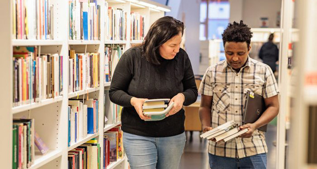 Två personer plockar böcker i ett bibliotek.