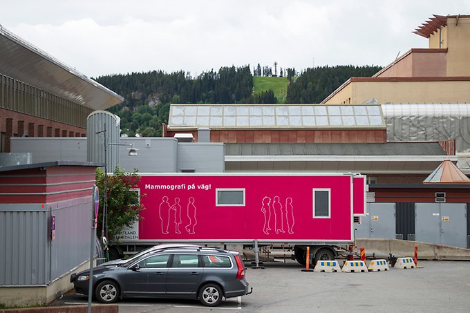 En stor vagn med rosa väggar och texten Mammografi på väg står uppställd på en parkering utanför Östersunds sjukhus. Framför vagnen står några personbilar parkerade.