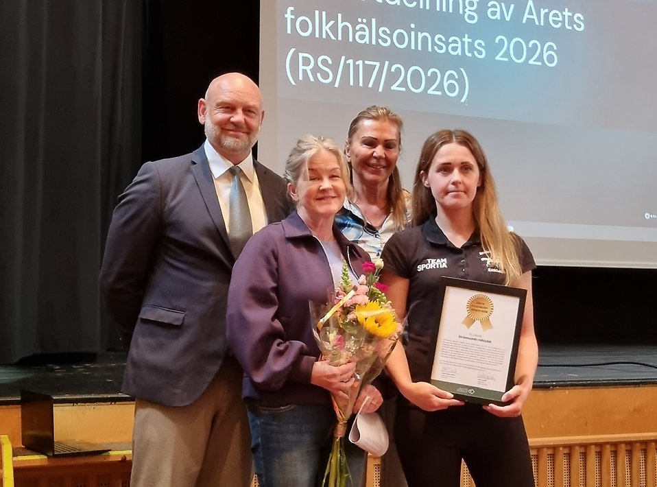 Fyra personer som står och tittar i i kameran. En håller en blombukett och en håller ett diplom.